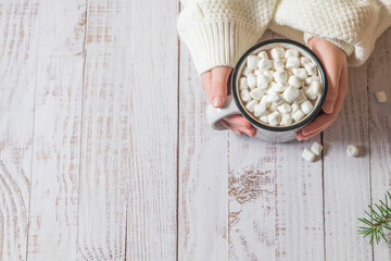 Person holds a mug of hot chocolate with marshmallows on top on a wooden background