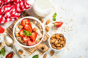 Oatmeal porridge with fresh strawberry and nuts on white background. Healthy breakfast. Top view with copy space.