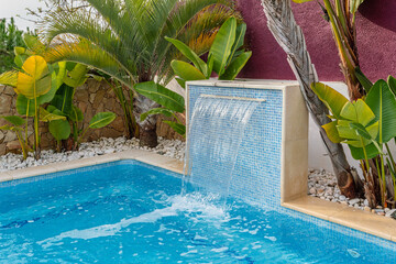 Close-up of a fountain waterfall in a luxury pool near the hotel with palm trees for tourists. - Powered by Adobe
