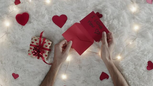 Mano di un ragazzo che scrive lettera d'amore per san Valentino su tappeto bianco
