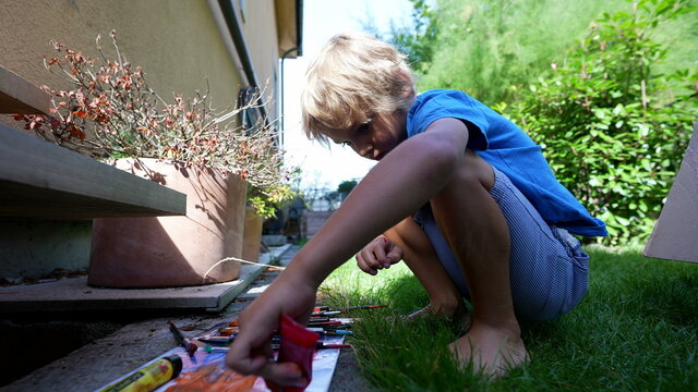 Artistic child playing with paint outside in home garden