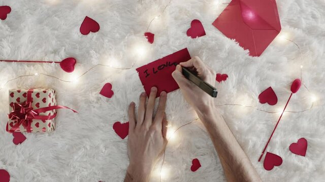 Mano di un ragazzo che scrive lettera d'amore per san Valentino su tappeto bianco