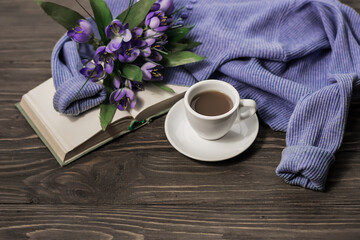 Obraz na płótnie Canvas Morning coffee. A cup of coffee on a wooden table, an open book and a warm sweater against the background of a bouquet of spring flowers. Still life concept. Cozy morning. 