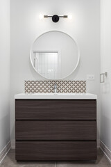 A wooden bathroom vanity cabinet with marble countertop, tiled backsplash, and a light over a...