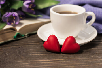 Fototapeta na wymiar Romantic morning. A cup of coffee, two hearts and a bouquet of flowers on an open book on a wooden table. Love, engagement and Valentine's Day concept. Copy space.