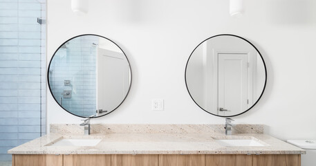 A long bathroom wooden vanity with granite countertops, circular mirrors, lights hanging from the ceiling, with a view of the blue tiled shower. - obrazy, fototapety, plakaty