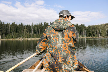 A young handsome man in a spoon fishing on the background of the lake. A guy in a jacket and a cap...