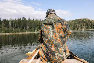A young handsome man in a spoon fishing on the background of the lake. A guy in a jacket and a cap...