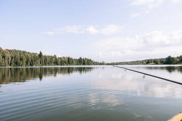A long fishing rod on the background of the lake. Fishing on a clear summer day on a beautiful lake.
