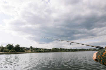 A long fishing rod on the background of the lake. Fishing on a clear summer day on a beautiful lake.