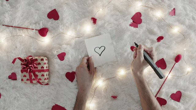 Mano di un ragazzo che scrive lettera d'amore per san Valentino su tappeto bianco