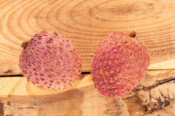 Two ripe sweet Litchi fruits on a wooden table, close-up, top view.