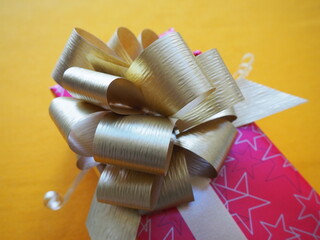 Red pink gift box with a large golden bow on a yellow ocher color background. Gift for Christmas,...