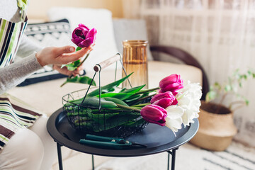 Woman making tulips flower arrangement at home. Fresh purple blooms picked up in basket. Interior and spring decor