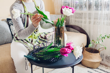 Woman puts bouquet of tulips flowers in vase with water at home. Fresh blooms picked up in basket....