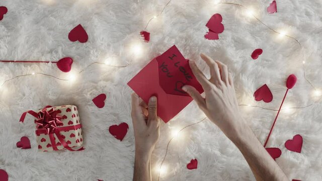 Mano di un ragazzo che scrive lettera d'amore per san Valentino su tappeto bianco