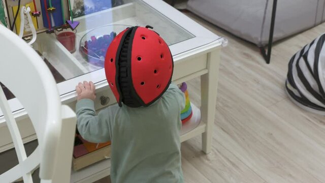 Baby wearing soft safety helmet learning to walk, craw sit and stand on the floor in living room, head protector helps reduce impact of falls on hard surfaces. High quality 4k footage