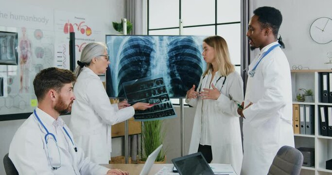 Workflow in clinic where pleasant successful high-skilled multicultural male and female doctors holding meeting and discussing results of chest and lungs x-ray,front view