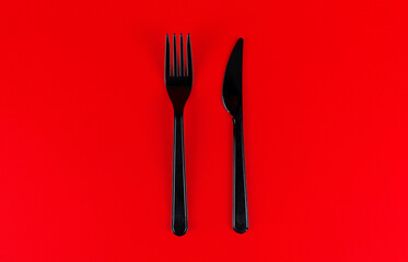 Black plastic fork and knife against red background