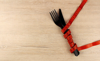 Plastic fork and knife wrapped with measuring tape on wooden background
