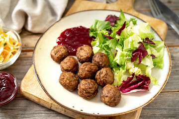 Swedish meatballs with salad and lingonberry jam in a bowl closeup. Traditional Scandinavian dish in a ceramic plate on a light gray wooden culinary background	