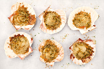 Backed scallops in shells on baked paper. Scallops au gratin on white plate. Mediterranean seafood. Fresh Shellfish. Aequipecten opercularis. Pecten Jacobaeus