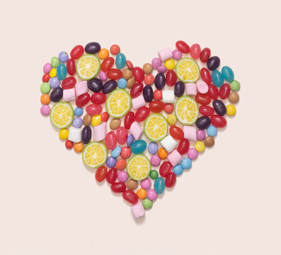 Sweet romantic minimal concept. Heart made of many different jelly beans and candies against champagne background.