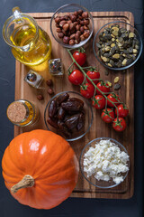 Whole Hokkaido pumpkin and curry, mini tomatoes, hazelnuts, pumpkin seeds, dates and feta cheese on a dark rustic background for gratinating.