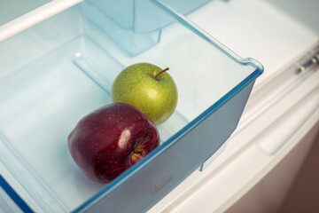 Empty open domestic refrigerator with 2 juicy and ripe and fresh apples in container. Green and red apple. The concept of diet and weight loss. Dietary healthy fruits for snack.