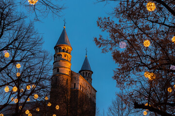 Maastricht, Netherlands 12-15-2021 Basilica of our Lady decorated with illuminated lights around hanging in trees during blue hour, creating a fairy tale setting while looking through the branches