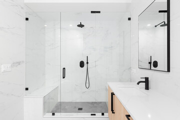 A beautiful luxury, modern bathroom with a light wood cabinet, walk-in shower with marble tiled...