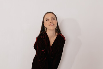 Fototapeta premium Charming adorable woman in stylish dress and wearing golden earnings smiling at camera over isolated backdrop. Calm happy brunette woman is looking at camera and laughing 