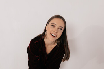 Fototapeta premium Smiling happy girl in festive dark dress laughing at camera while posing over isolated backdrop. Stylish happy woman preparing for party 