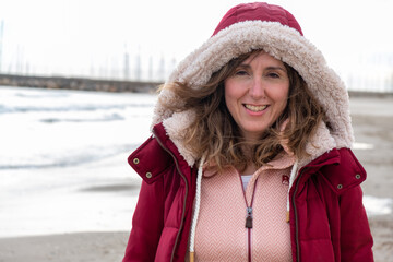 Happy Baby Boomer woman in red hooded coat on the beach in winter