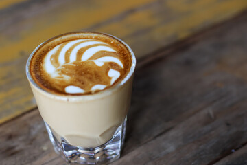 Hot coffee latte art in cup on wooden table.