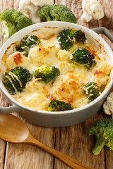 Gratin made from broccoli, cauliflower with bechamel sauce in a pot close-up on a wooden table. Vertical