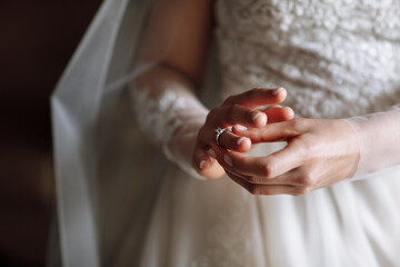 cropped photo of gentle hands of the bride standing in a white lace dress puts a wedding ring on...