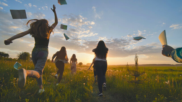 Cheerful Students Run Throwing Notebooks After School At Sunset.