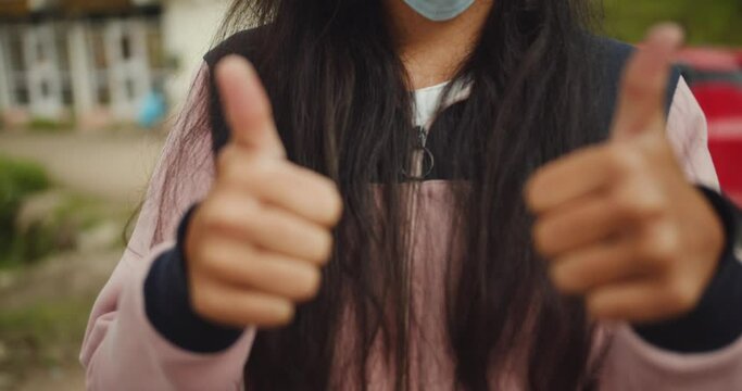 A shallow focus of an Indian female wearing a facemask showing two thumbs up