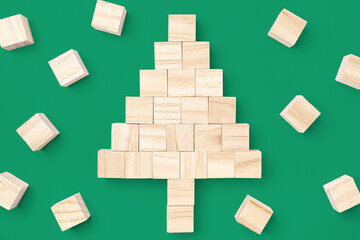 Wooden cube block stacking into a Christmas tree surrounded by small wooden cubes isolated on green background, concept of Christmas, happy new year.