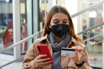 Credit card payment outdoors. Beautiful young woman with black protective mask enters her credit...