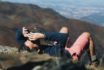 Hiker lying on the mountaintop and looking into the sky through binoculars