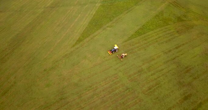 Top down view of the agriculture machinery during haymaking. Flying over the field and tractors.