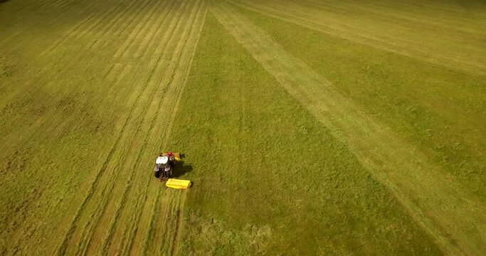 Top down view of the agriculture machinery during haymaking. Flying over the field and tractor.