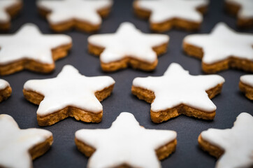 Christmas pastry recipe. Freshly baked cinnamon stars with icing or sugar glaze on a background made of black slate.