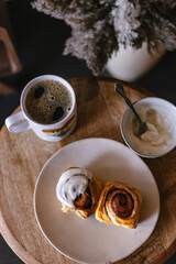 Baked cinnamon bun rolls with white vanilla bean cream frosting. Moody dark food photo. Coffee and baked pastry breakfast. Fresh baking treat. Brown cinnamon sugar. Swirls on roll. Coffee table.Brunch