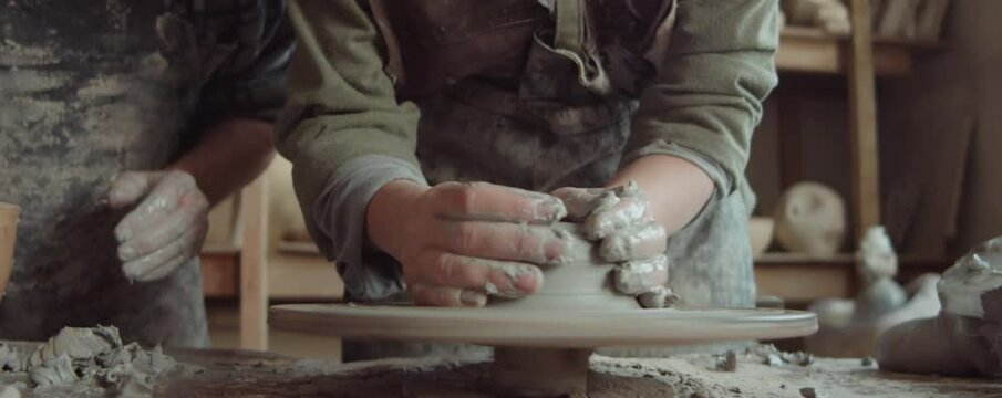 Close up tilt up shot of young cheerful woman wheel throwing and smiling while taking pottery class in workshop