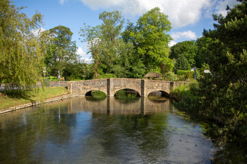 Fototapeta na wymiar Beautiful small bridge over calm water and green trees in summer at Arlington, UK