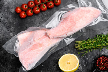 Red Snapper frozen pack fish meat, with herbs, on black dark stone table background, top view flat...