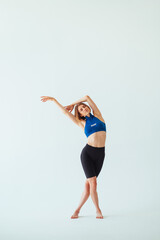 Fototapeta premium Attractive woman in sportswear stretching on a white background in the studio, stretching to the side. Vertical.